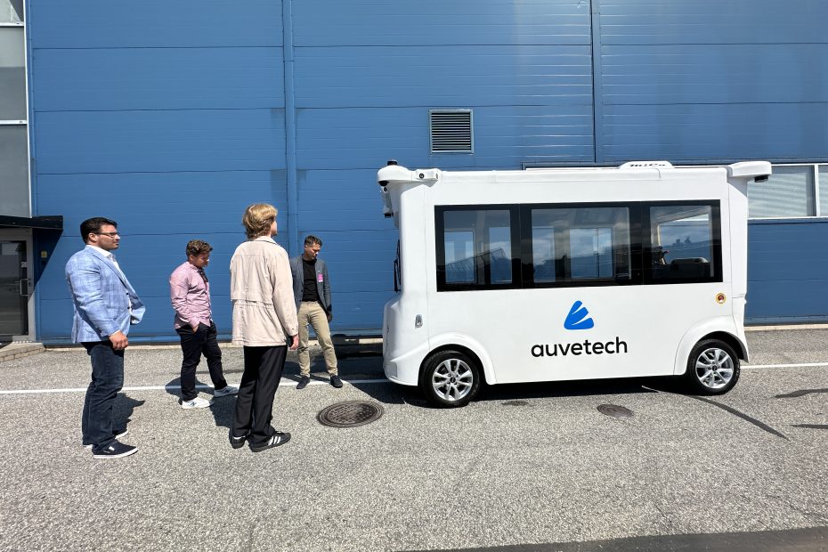 Henkilöt katselevat Auvetechin autonomista valkoista sähköbussia