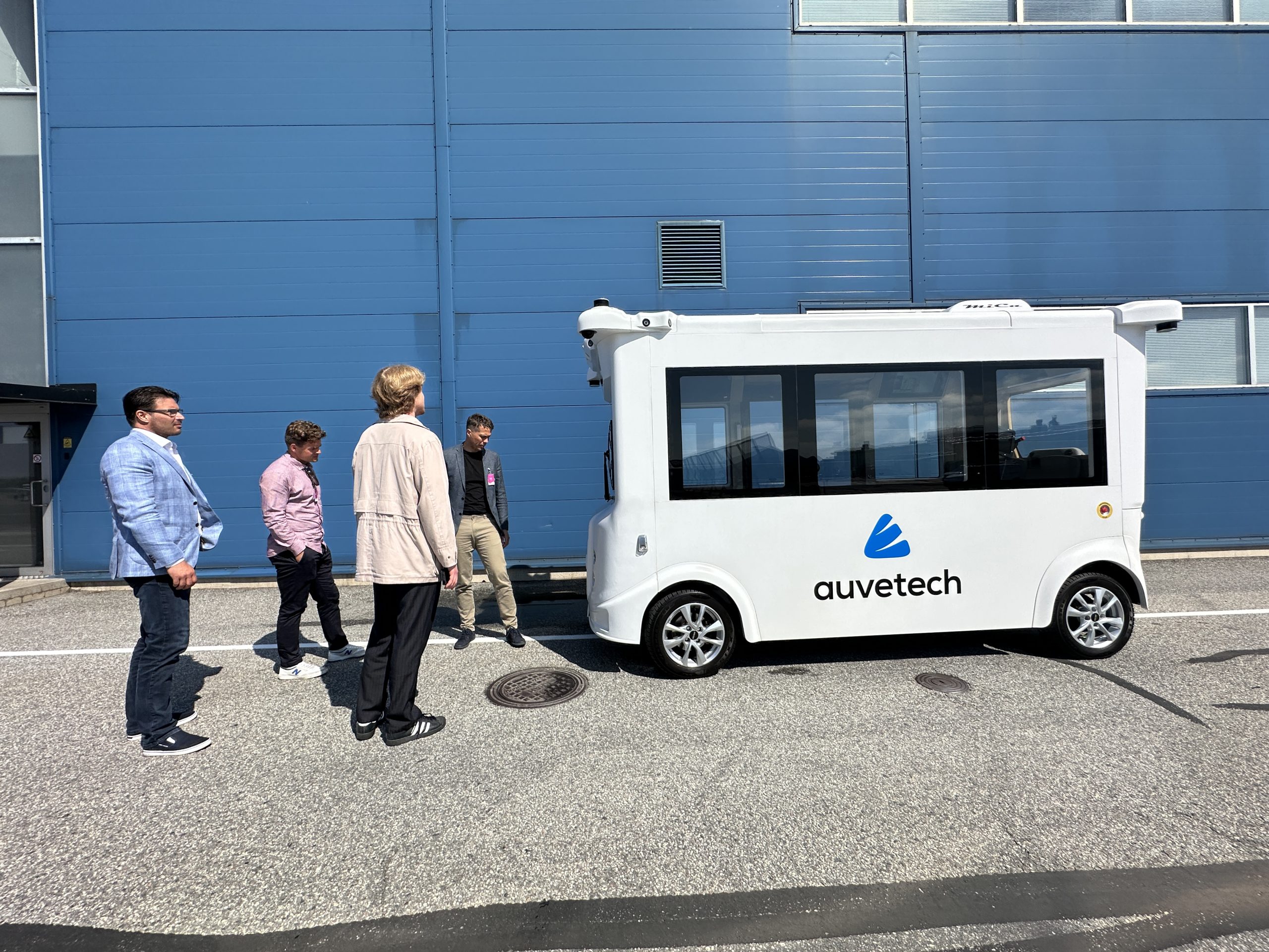 Henkilöt katselevat Auvetechin autonomista valkoista sähköbussia